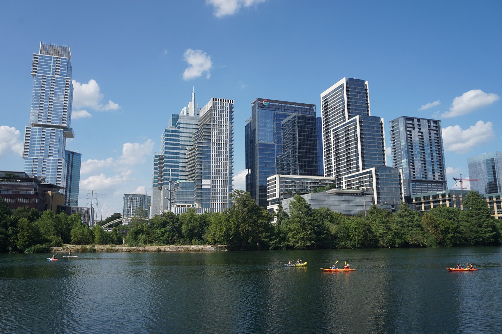 The downtown Austin skyline seen across Lady Bird Lake, with kayakers on the water and trees along the bank