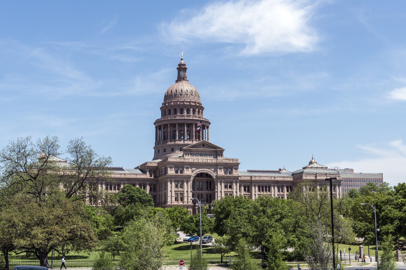 The pink granite Texas State Capitol in Austin with its dome, seen across the tree-filled grounds